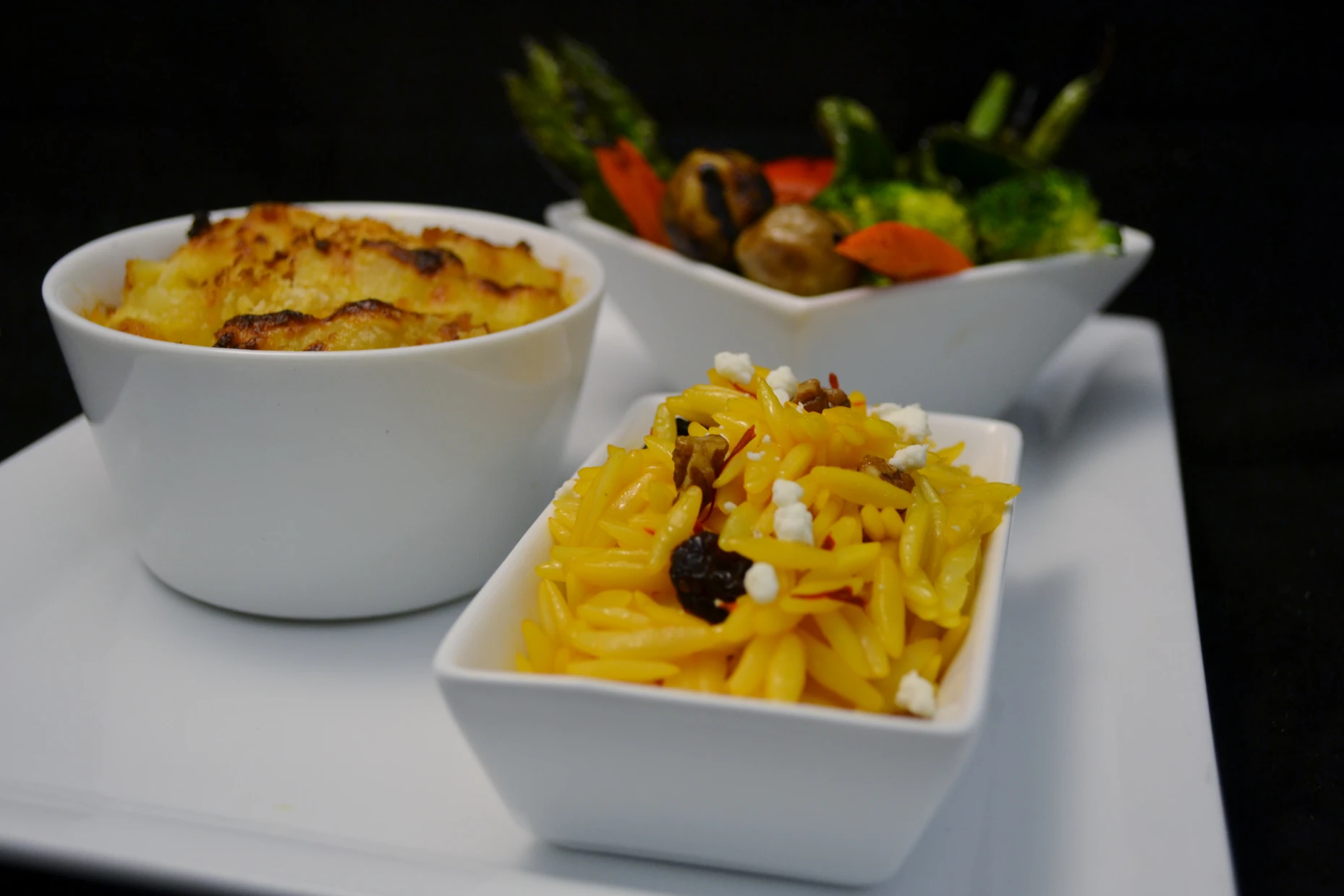 Potato gratin, saffron orzo and grilled vegetables in white bowls