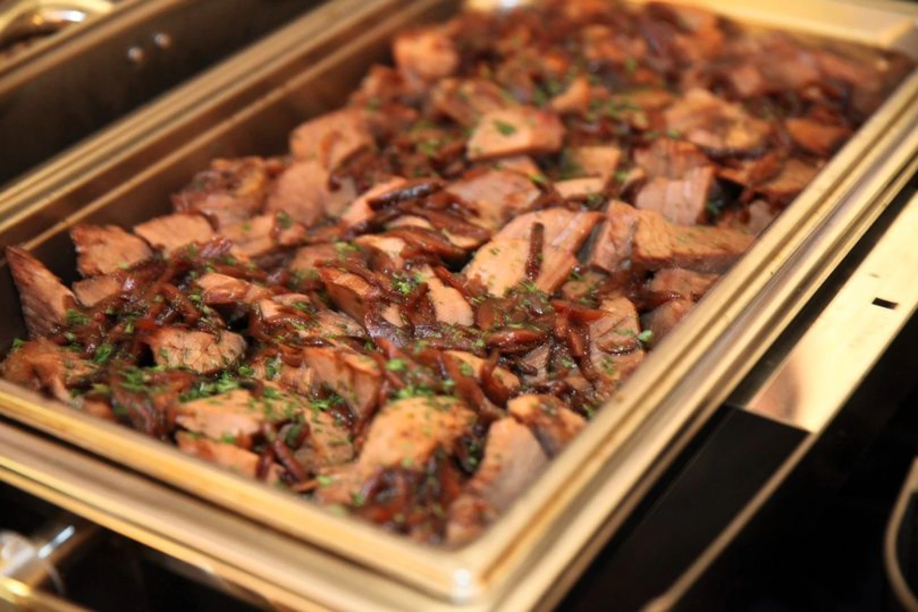 Chafing tray of sliced beef with caramelized onions and herbs